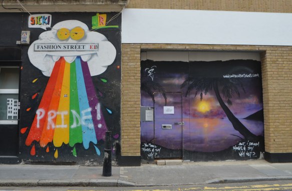 two murals. on the left, a large white cloud with yellow eyes and three white upper teeth is spitting out a rainbow that someone has written pride on the top of . The other mural is a sunset scene with a palm tree and beach in silhouette in the foreground, purple sky and water, yelloish orange sun and reflections in the water. 