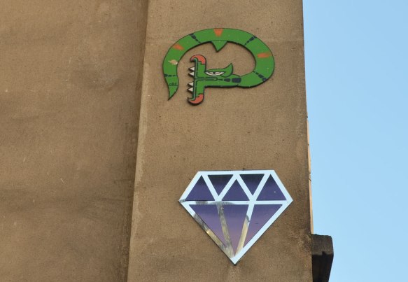 two graffiti pieces on a wall, a blue and silver diamond shape an a green snake 