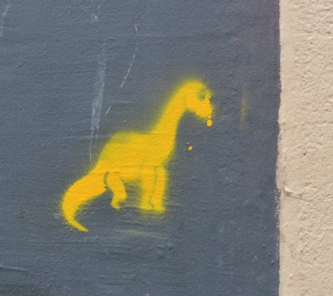 stencil graffiti of a little yellow dinosaur 
