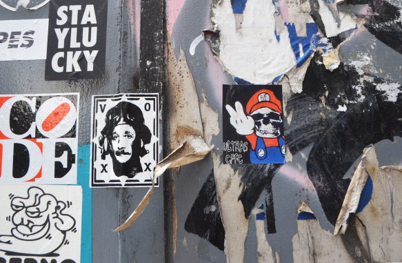 stickers and paste ups graffiti on a wall, Mario brothers parody, man by voxx, 