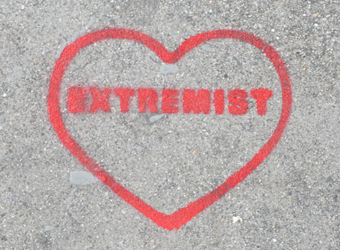 red stencil on grey concrete sidewalk, outline of a heart with the word extremist written inside it. 