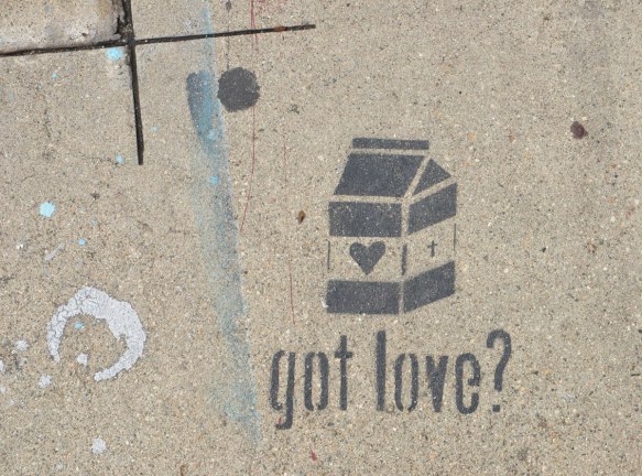 black stencil on grey concrete sidewalk, of a small milk box with a heart on the side. Words written underneath are got love?
