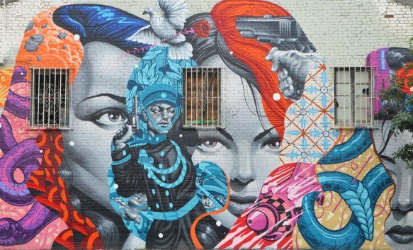 part of a larger mural, two women's faces with a man in a black and blue outit between thwm, a white dove is strating to take flight between their foreheads, a pistol is aimed at the dove, 