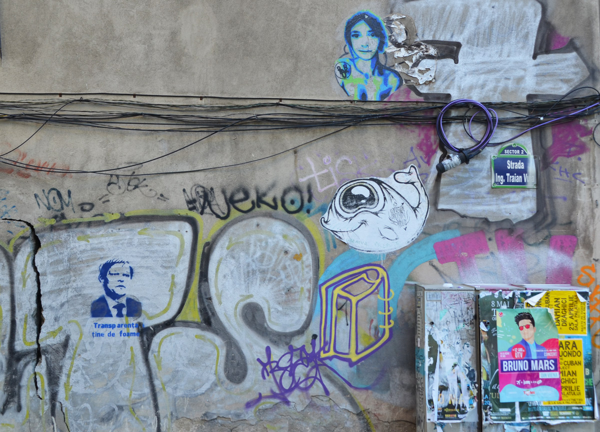 small pieces of graffiti on a wall, a paste up woman, a paste up fsh, a stencil head with words, also a poster for a Bruno Mars concert 