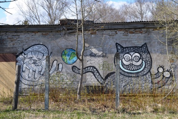 street art by multistab. A blue and green small plaet earth in between two large black and white creatures. One looks like a grinning cat, the other might be a cat but migh be something else