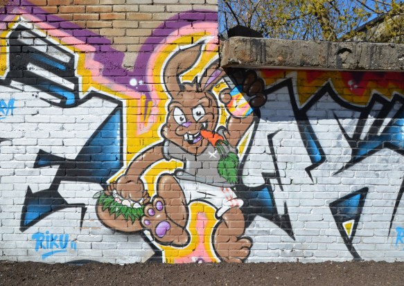 painting of a large agressive stylized rabbit in grey top and white shirts, a carrot in its mouth, running on two legs, one arm upraised.