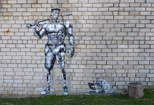 a large muscular partially clad man with a weapon over his shoulder, on a grey brick wall, a small hedgehog is working on a laptop beside him. graffiti