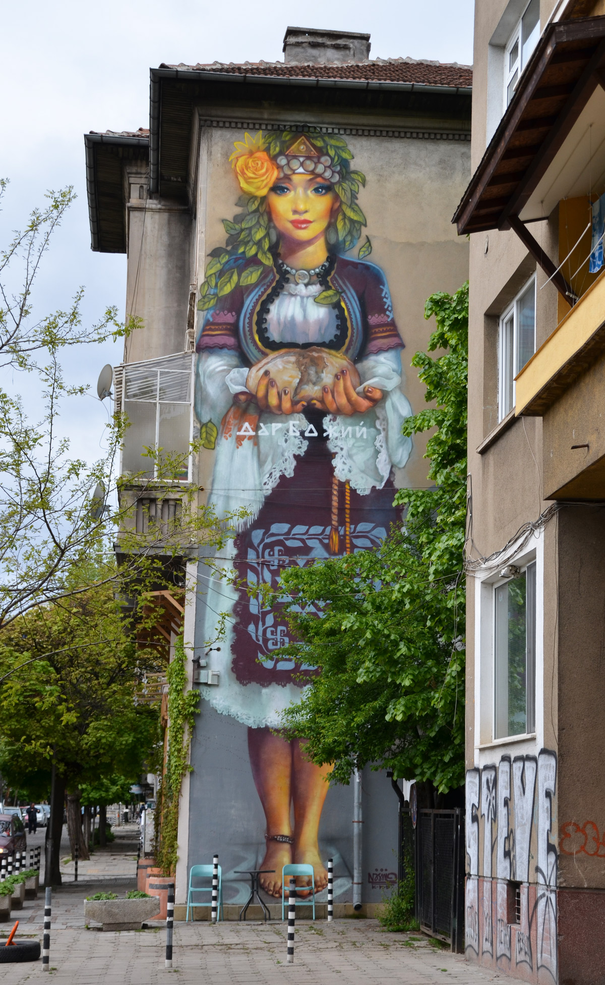 mural by street artist massimo on the side of a building in Sofia, mural is about 3 storeys high. Woman is dressed intraditional Bulgarian costume 