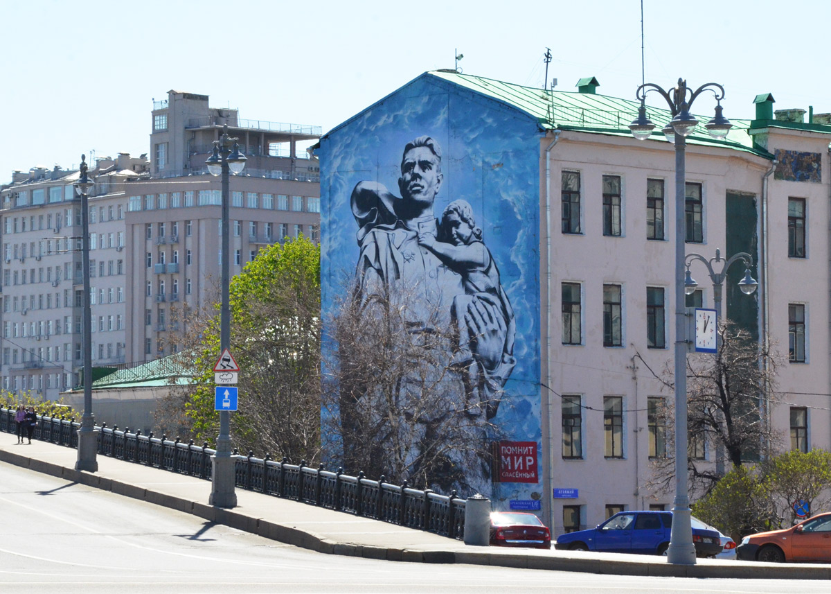 large mural, blue background, man with child on his back looking over his shoulder 