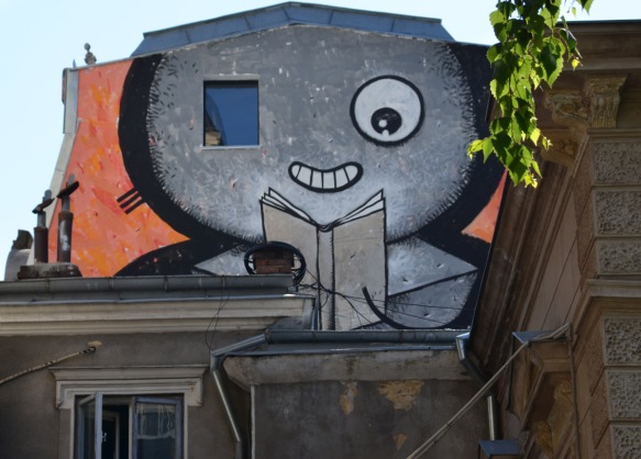 large mural of a grey face reading a book. One of the eyes is actually a window 