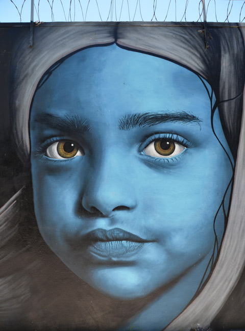 close up a large girl's face painted blue in a large mural, greenish eyes, head scarf on her head 