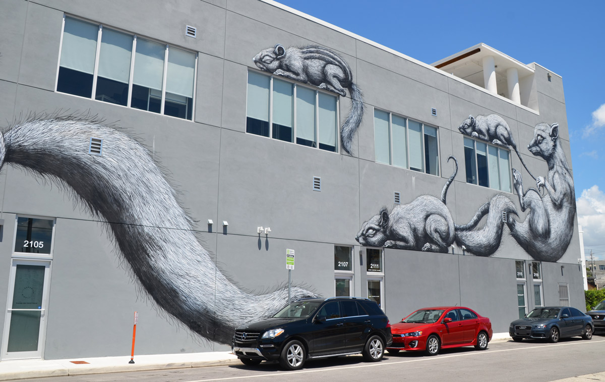 three cars parked in front of a large black and white mural on a grey building, by ROA, two adult animals and two babies 