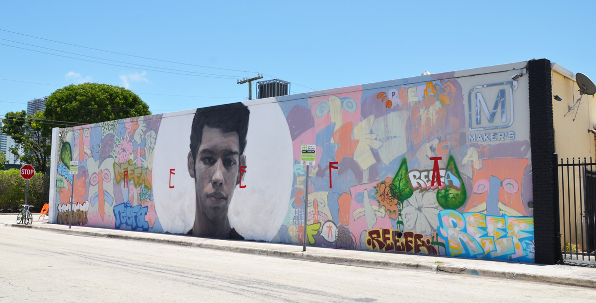 long horizontal mural by Axel Void with a young man's head inside a white circle in the middle, the edges are faces in pastel colours, stylized