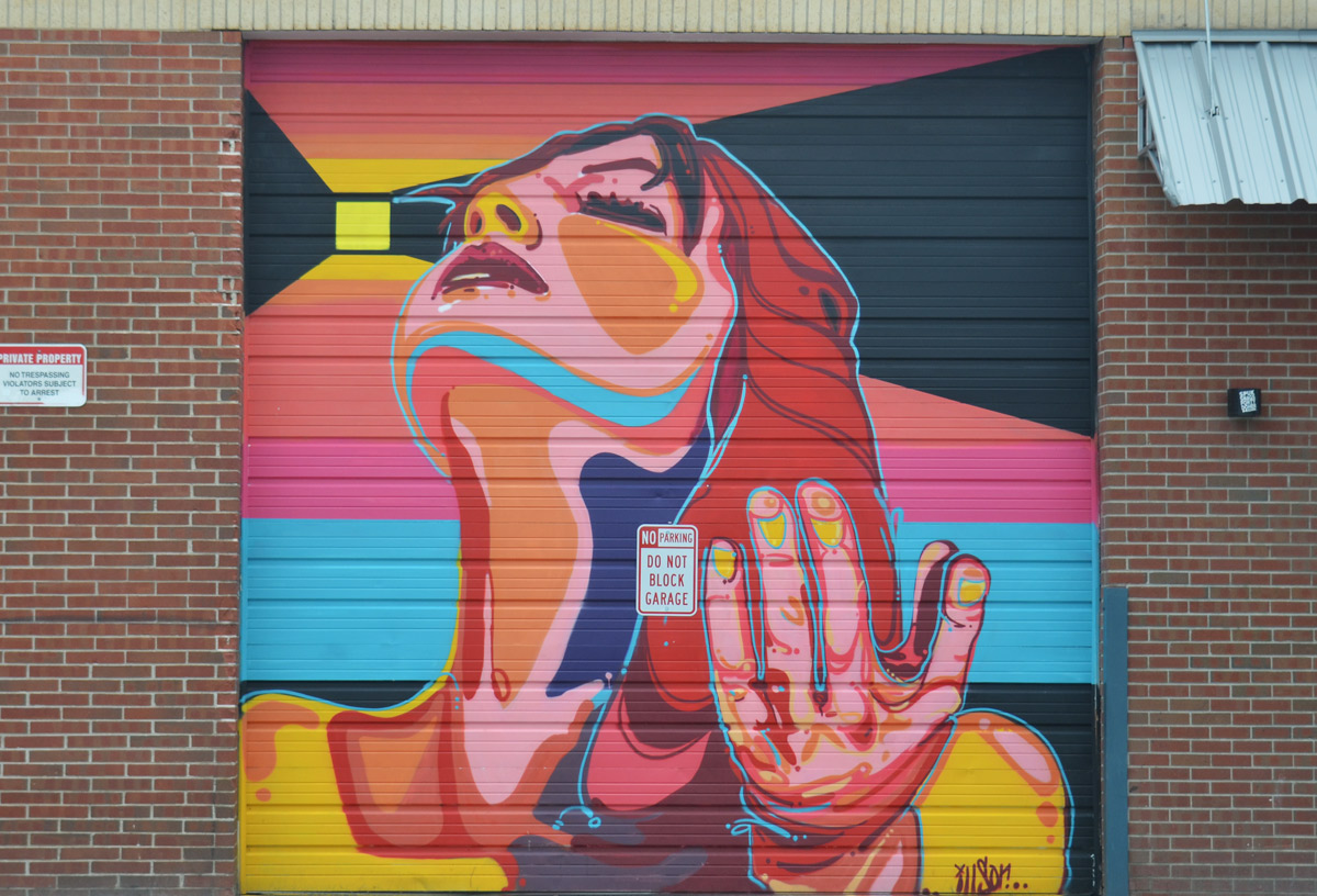 colourful mural on a garage door by illson in denver of a woman looking upward, with one of her hands raised up a bit