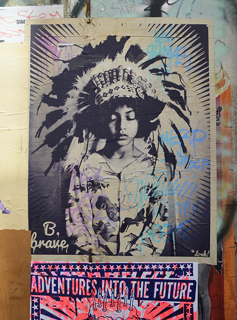 be brave pasteup by donk, ofLondon, in Bristol a young person with eys closed, Indian feather head dress on hed, in monotone black and white 