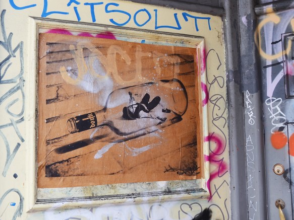 donk pasteup in a doorway, on brown paper, a drawing of a man lying on his back inside a liquor bottle, he's holding another bottle in his hand