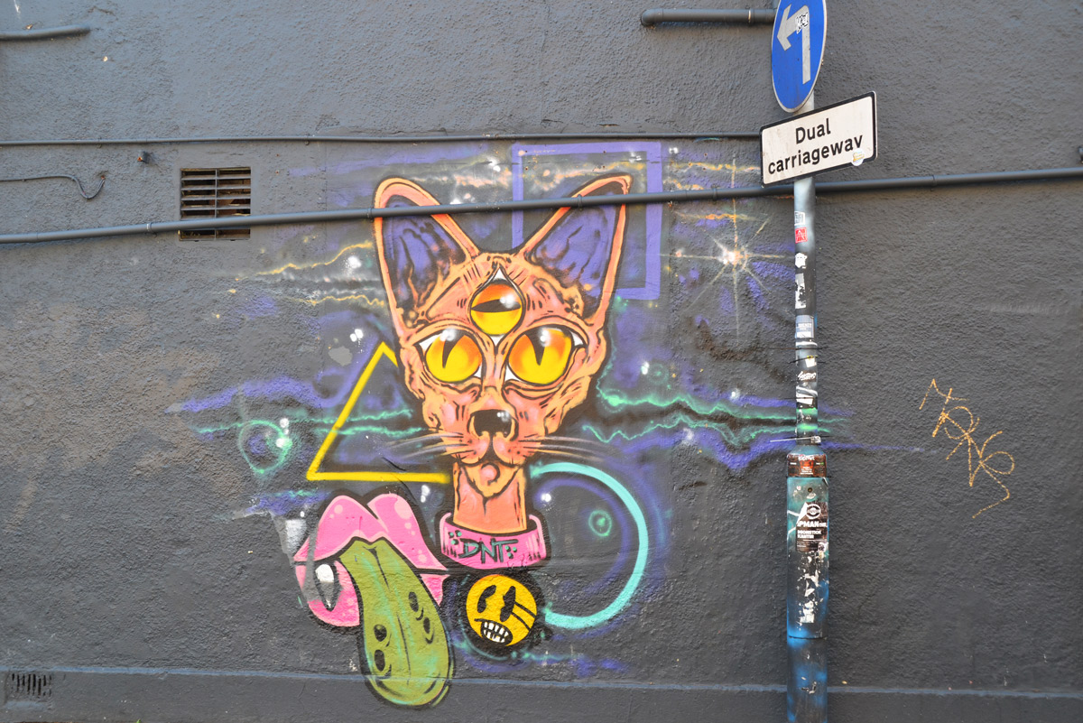 graffiti, cat head,red lips with green tongue sticking out, plys yellow triangle and blue circle