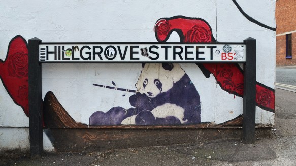 small street art piece of a panda with bamboo in its mouth, under a street sign for Hillgrove Street 