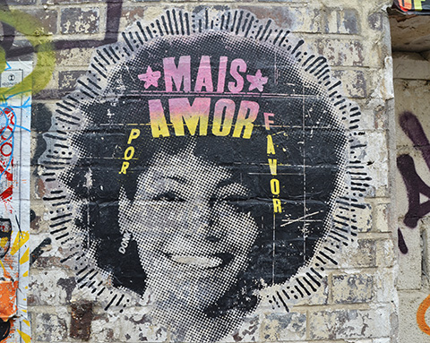 pasteup of a smiling woman's head, large puffy hairdo, words say mais amor por favor. 