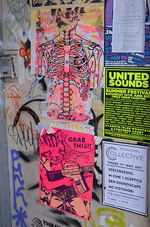 two pink paste ups on a door - the top is a drawing of a ribcage, bones only and the other is a cat with a gn and the words grabthis (grab this pussy?)