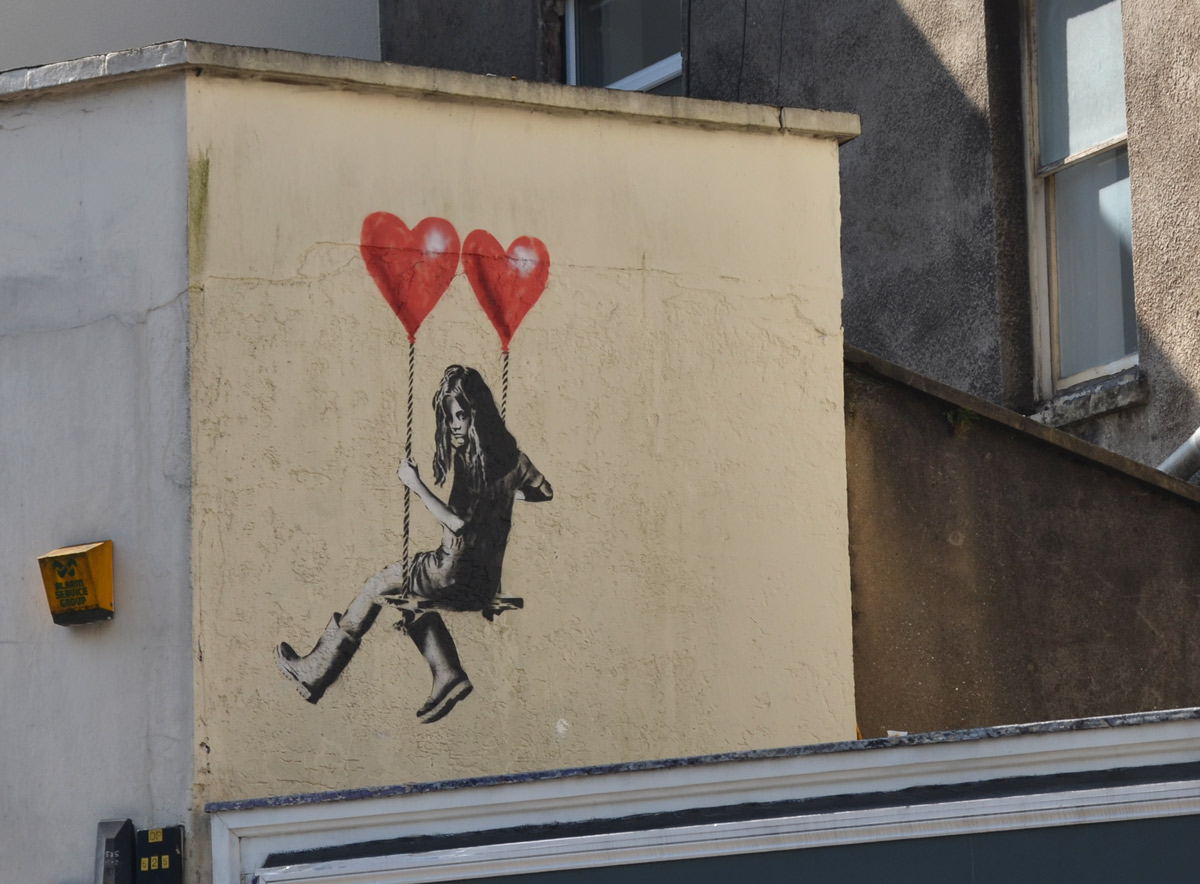 street art piece of s girl sitting on a swing that is being held up by two red balloons