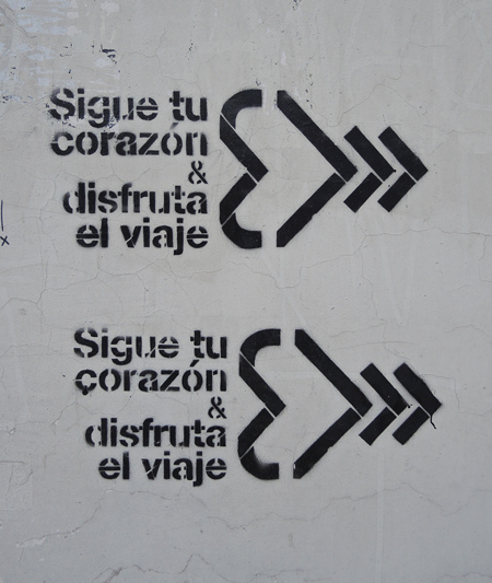 black stencil on grey concrete, sigue tu corazon a disfruta la viaje, written twice 