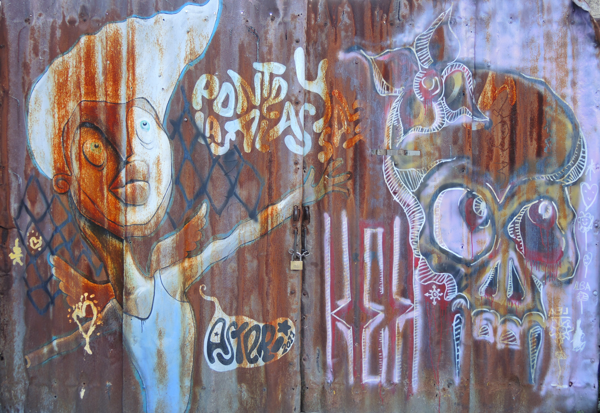 on a rusted metal gate that is locked closed, graffiti of a person with outstretched arm, as well as a skull 