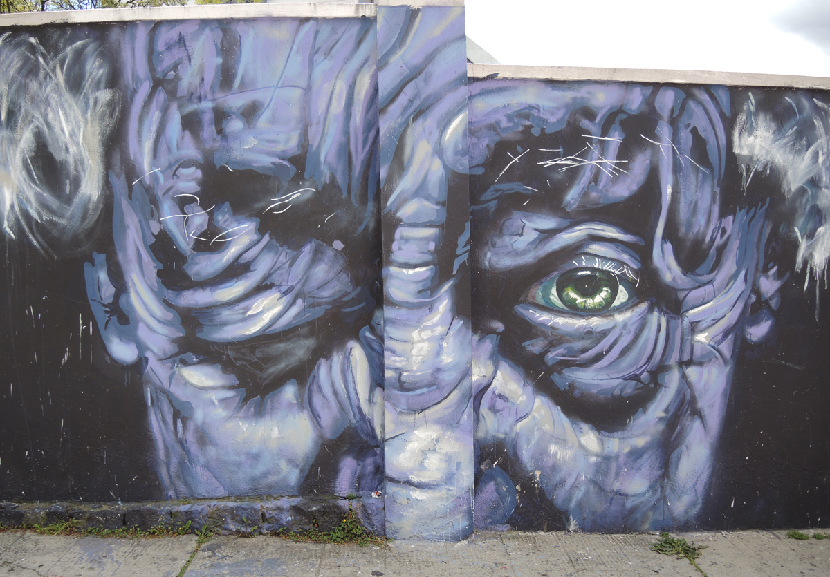 realistic, and large, painting of a wrinkly man's face, one eye open and one closed. The open eye is green. 