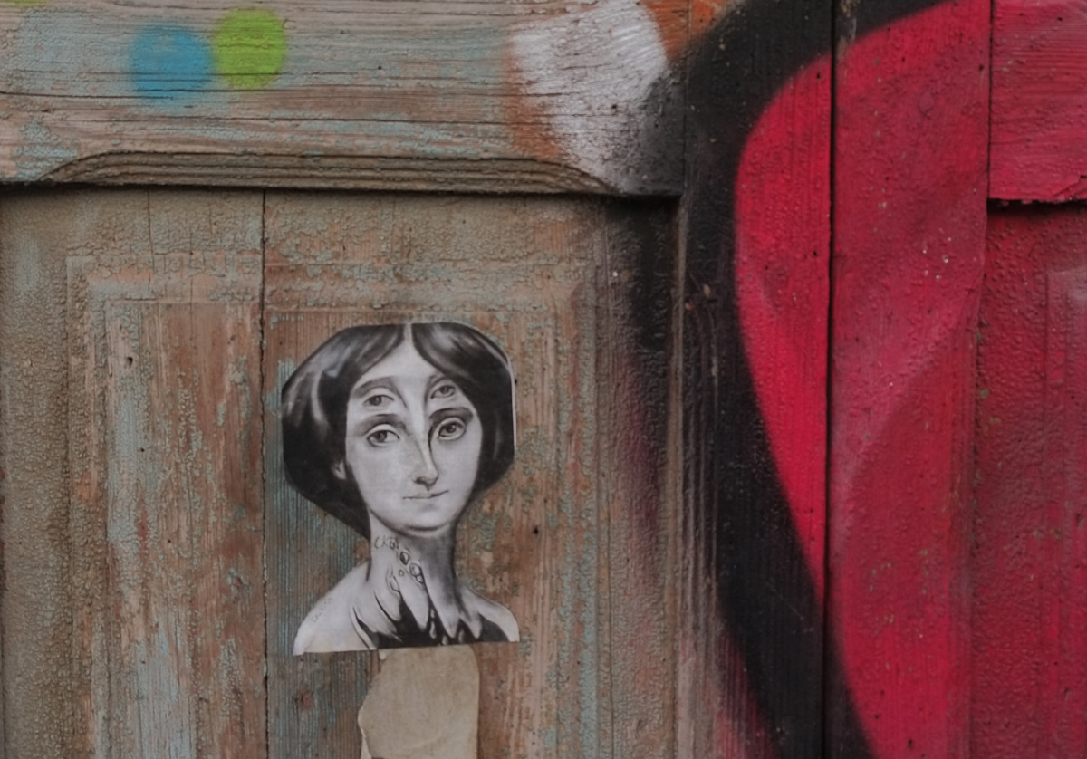 black and white paste up by CKTN on a wooden door of a woman's head, she has 4 eyes, 