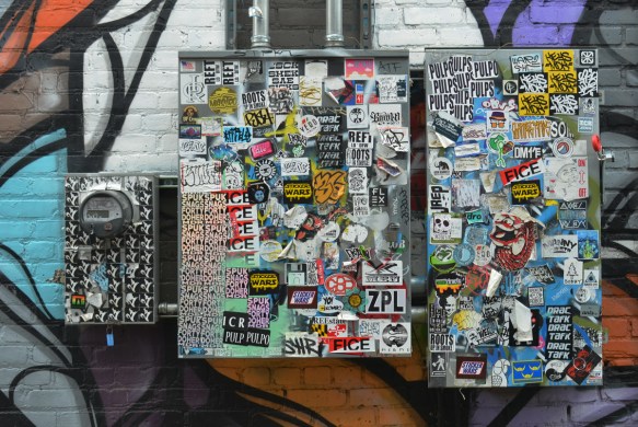 two metal boxes outside and a meter box, all covered with stickers 