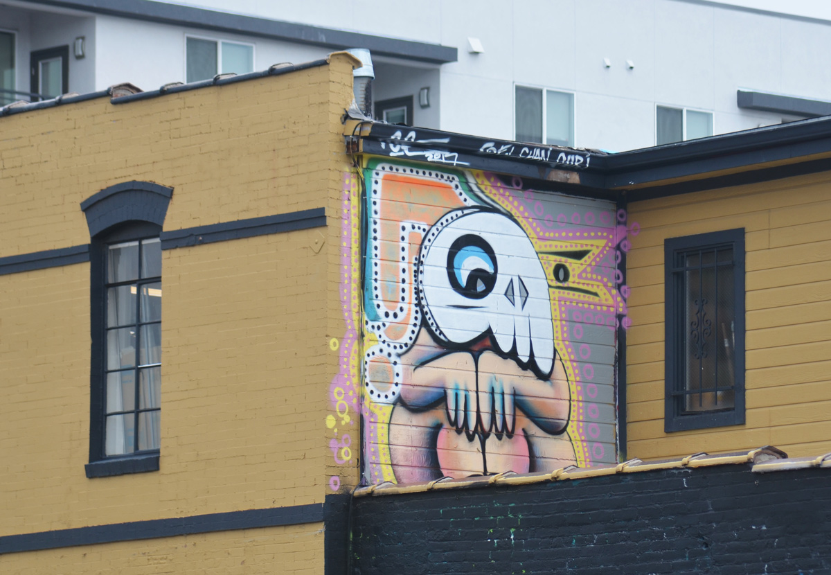 a small mural on an upper storey wall of a small person, naked, sitting with knees up, wearing a large white animal mask 