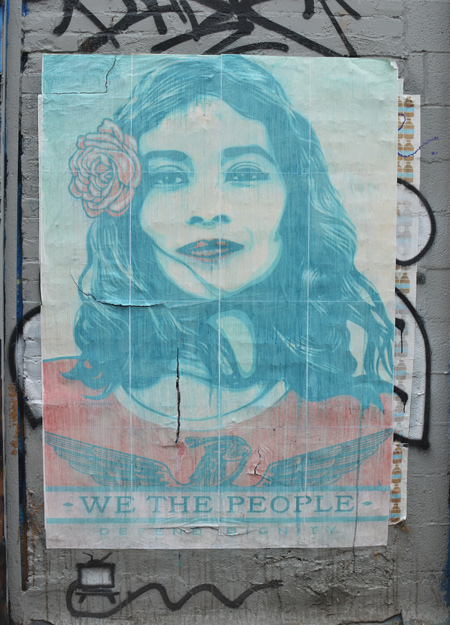 faded poster on an exterior wall, picture of young woman with flower in her hair and the words we the people 