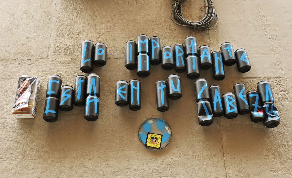 empty cans covered with black and each with a blue letter on them, the cans are put together on a wall so the letters make words. 