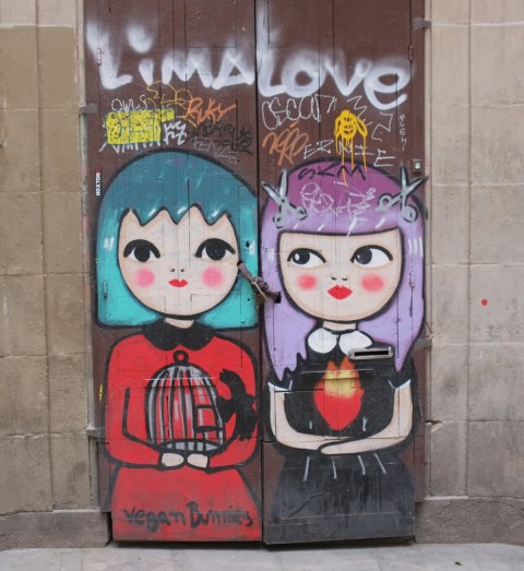 street art painting of two young women on a door, stylized, one with turquoise hair and the other with light purple hair. One with a red dress and holding a bird cage that a bird is flying out of. words at bottom say vegan bunnies. scrawled across the top are the words Lima love. 