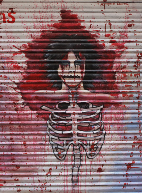 painting on a door of a person's head, with lots of black hair, top of body is just rib cage with lots of red paint that looks like blood splattered all over it 