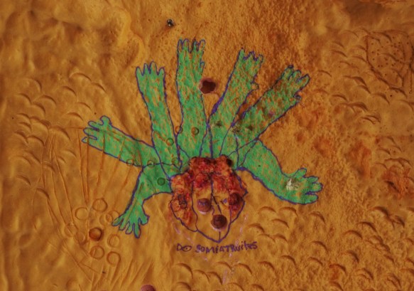 small painting on a gold coloured wall, exterioe, six green arms with fingers stretching out from a central reddish face 