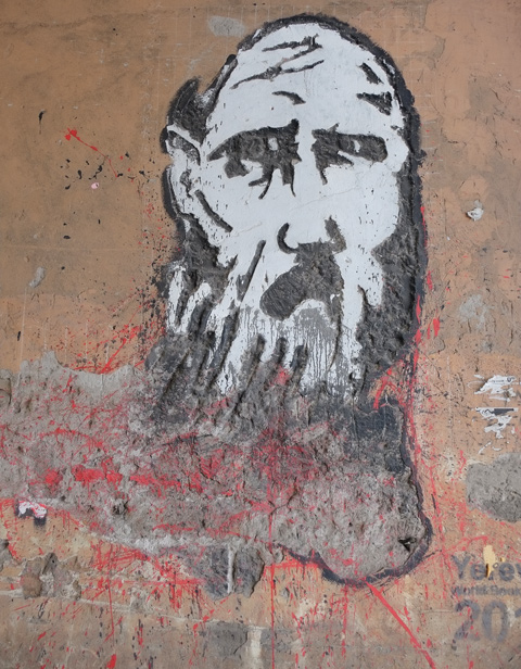 yerevan street art, man's head, black hair and beard and moustache, wild eyes, on concrete that is crumbling a bit 