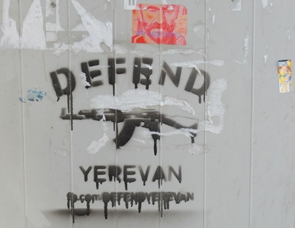 stencil of a rifle with the words defend yerevan around it, also a sticker of a man's face in pink and orange that says with Pavel on it. 