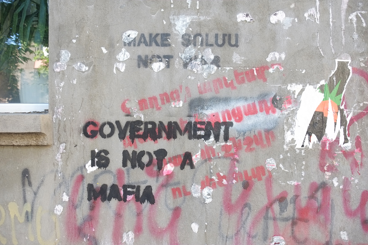 word stencils on top of each other on a wall, one in black says Government is not a mafia, red words in Armenian