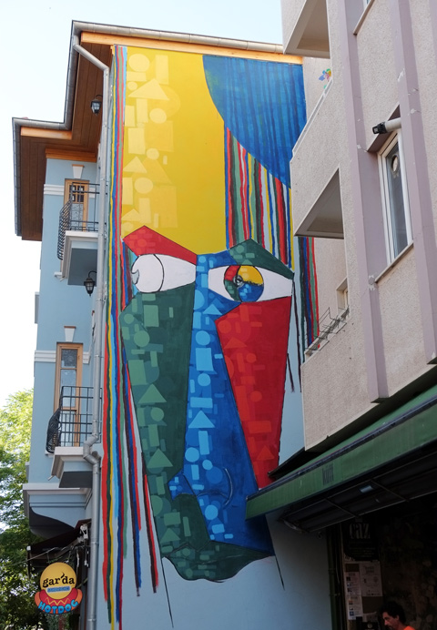 large mural in Kadikoy of an abstracted face in yellow, blue, red, and green, eyes looking out onto the street 