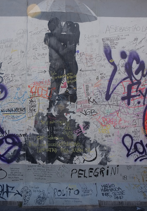 part of a mural on Berlin Wall, Eastside gallery - lots of graffiti, a pasteup of a couple kissing under an umbrella