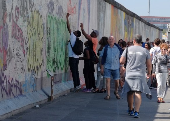 people reaching up high to write things on the wall, part of a mural on Berlin Wall, Eastside gallery