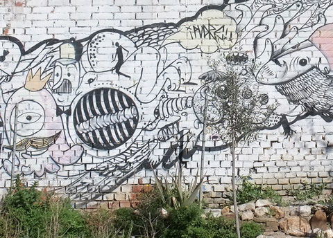 close up detail of mural on white brick, trees and plants in front 
