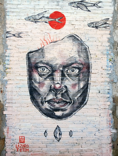 large realistic painting of a man's face on white brick wall, with some fish swimming above his head, signed as 