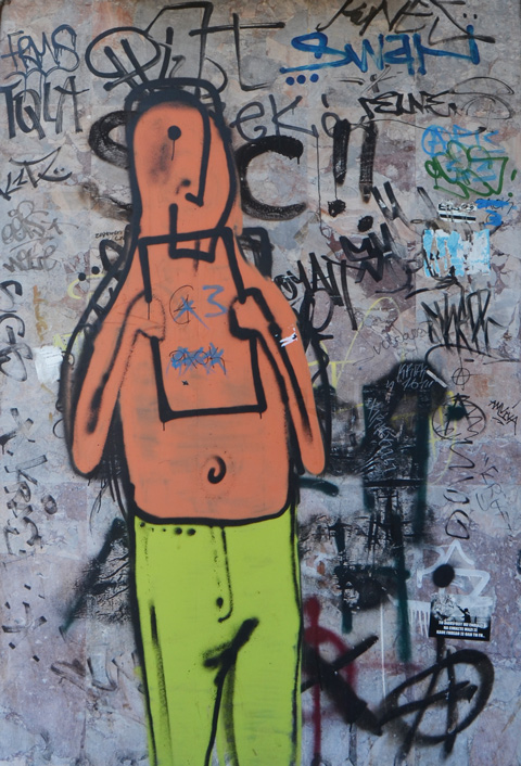 black line drawing of a man on a graffiti covered door, top painted orange and bottom of man painted green 