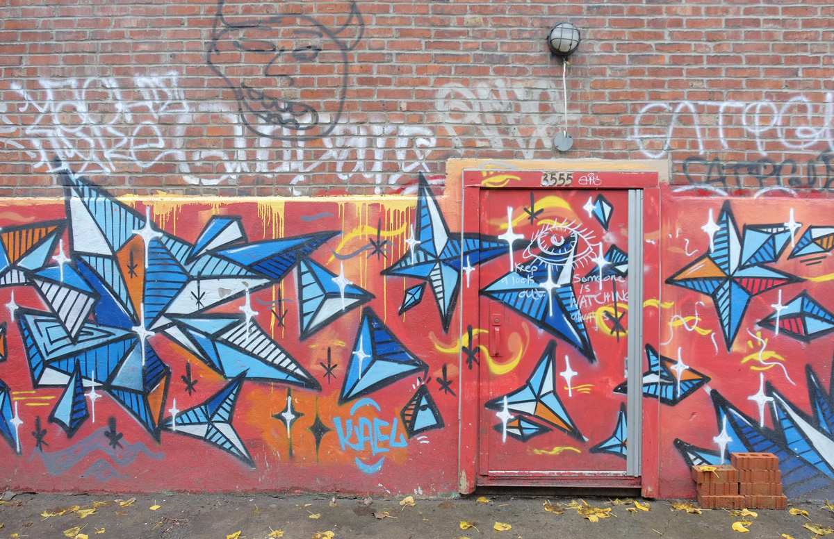 mural, red backgound across back of brick building and door, shapes made from blue triangles painted on the red 