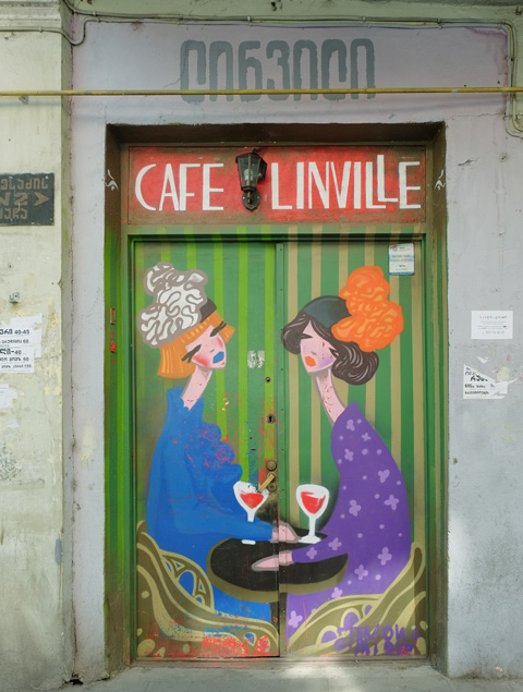 closed and locked double doors painted with two women talking over glasses of red wine, with the words Cafe Linville written across the top of the painting