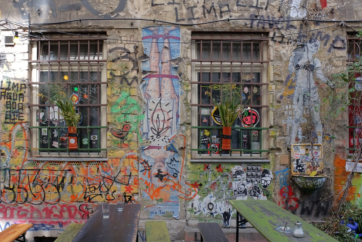 two windows on a wall, cafe tables in front of the wall, graffiti on the walls around the windows 