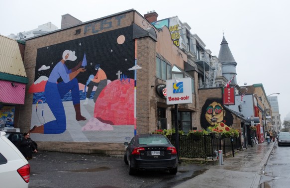 street scene, pizza restauarant, hotel, turret in the background, car parked in front of a mural