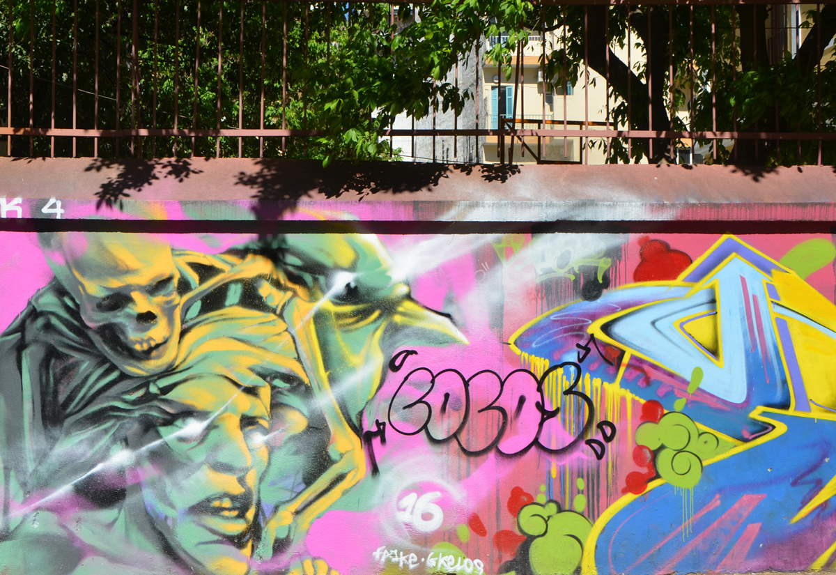 graffiti and street art on a low wall in Thessaloniki, with leaves of trees above the wall 